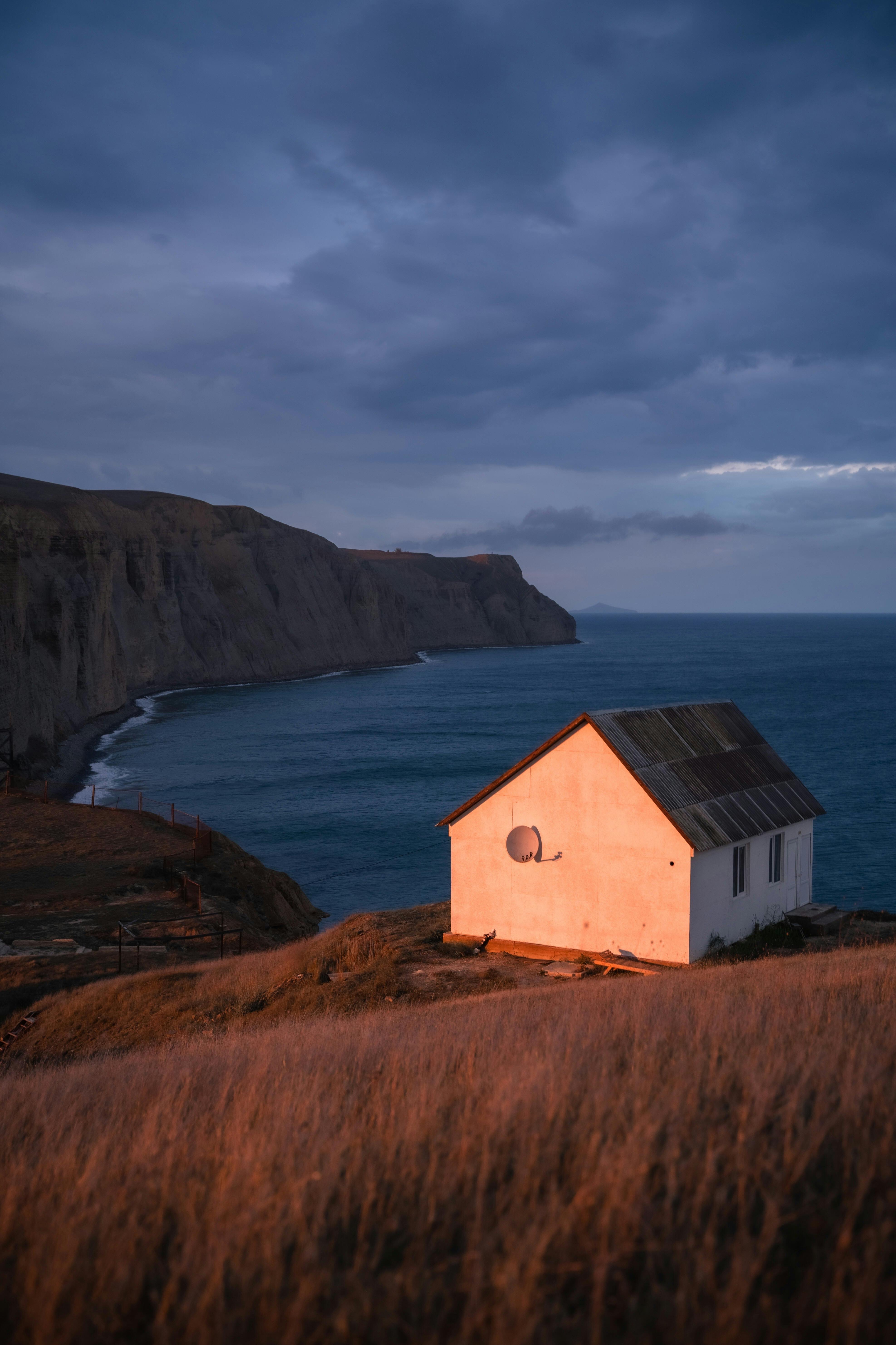 海岸悬崖上的一座孤独的房子被夕阳照亮，俯瞰大海