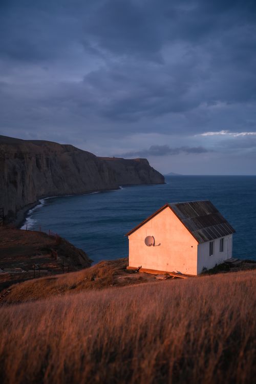 Free A lone house illuminated by sunset light on a coastal cliff, overlooking the sea. Stock Photo