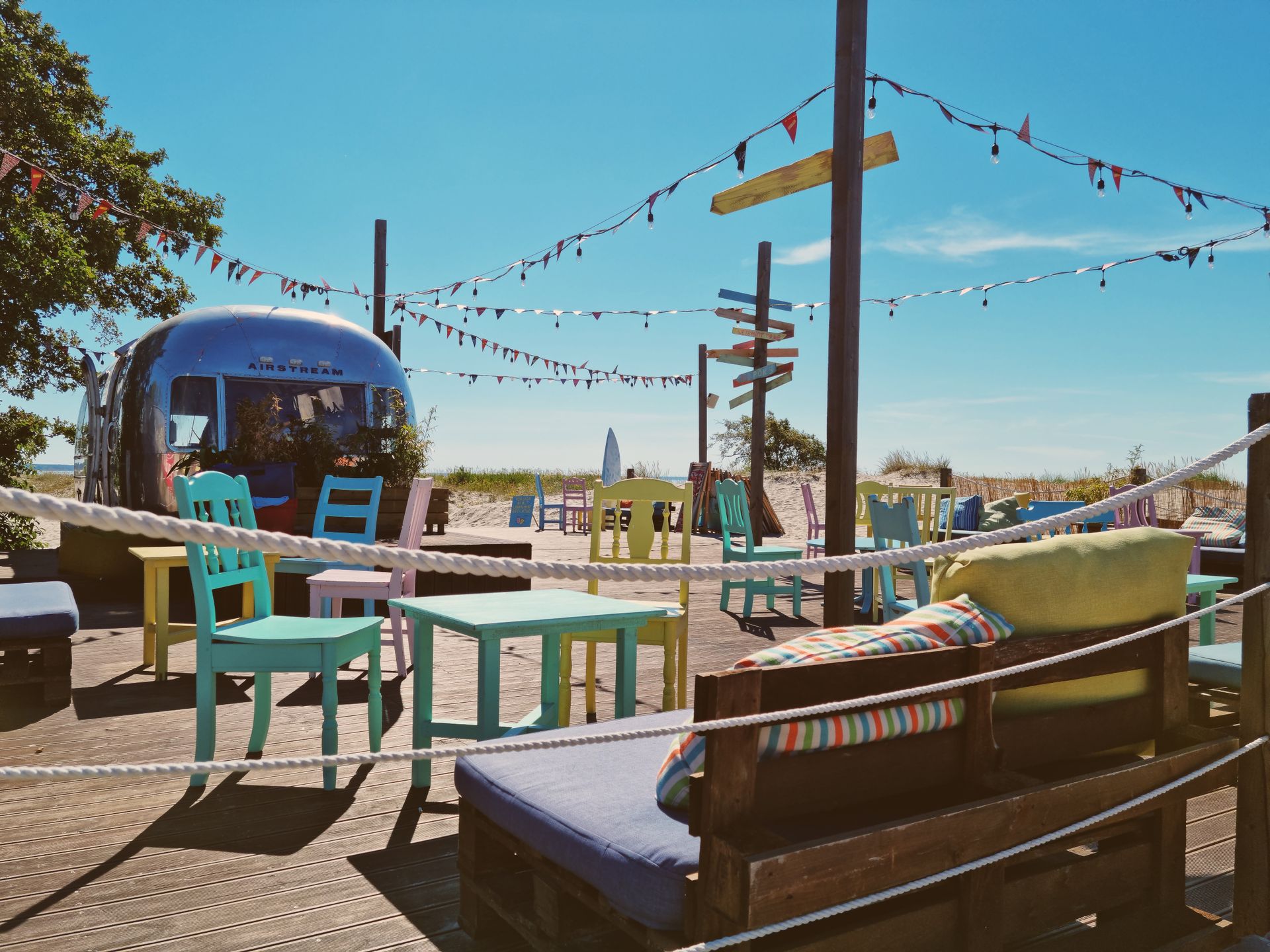 A vibrant outdoor cafe by the beach with colorful furniture and vintage decor, perfect for summer leisure.