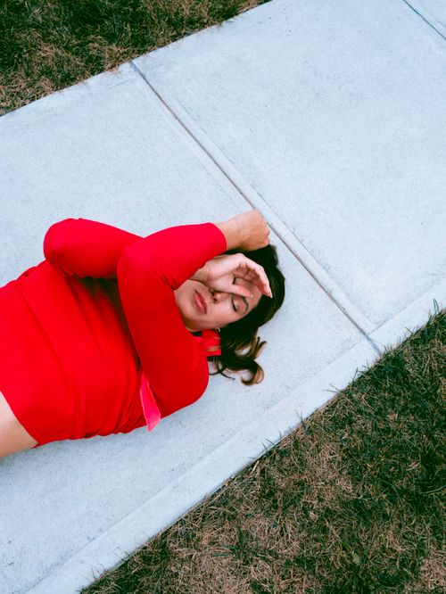 Free Woman in a red sweater lying on a sidewalk, expressing relaxation or contemplation. Stock Photo