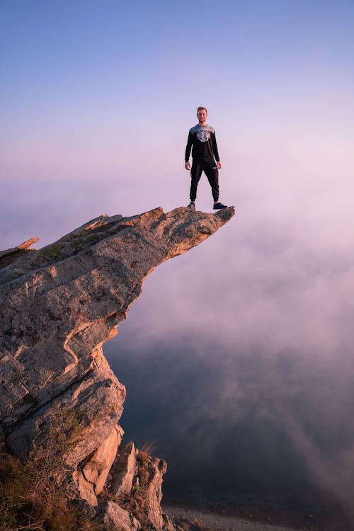 Free Man in Black Jacket Standing on Brown Rock Formation Stock Photo