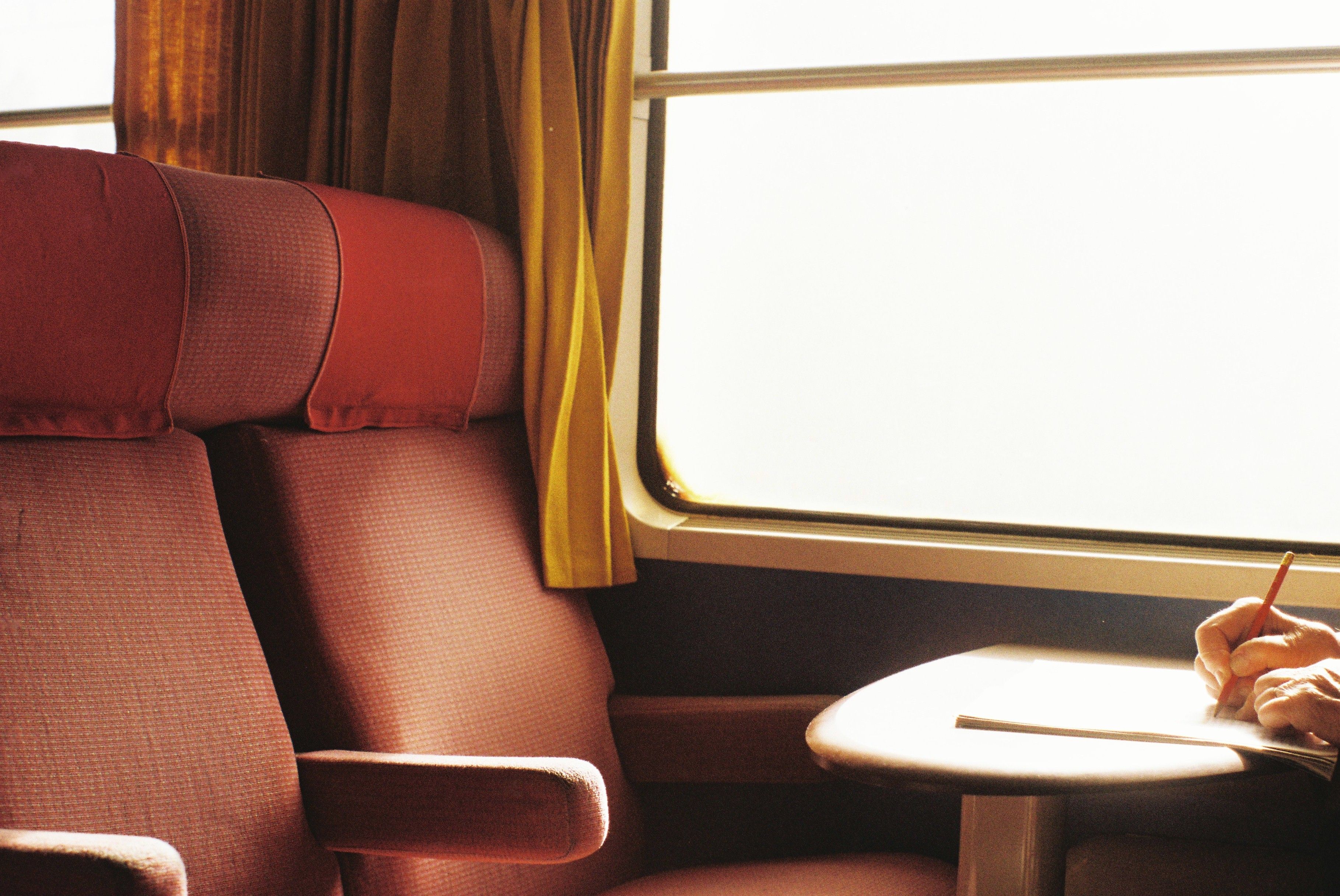 Train carriage seats beside a window and table, with a passenger writing in a notebook