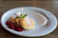 Top view of round plate with golden curd fritters decorated with powdered sugar and fresh mint near strawberry jam with whole berries and sour cream