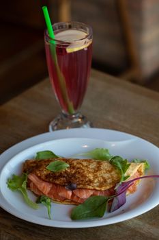 A delicious breakfast omelette served with a refreshing pink beverage on a wooden table.