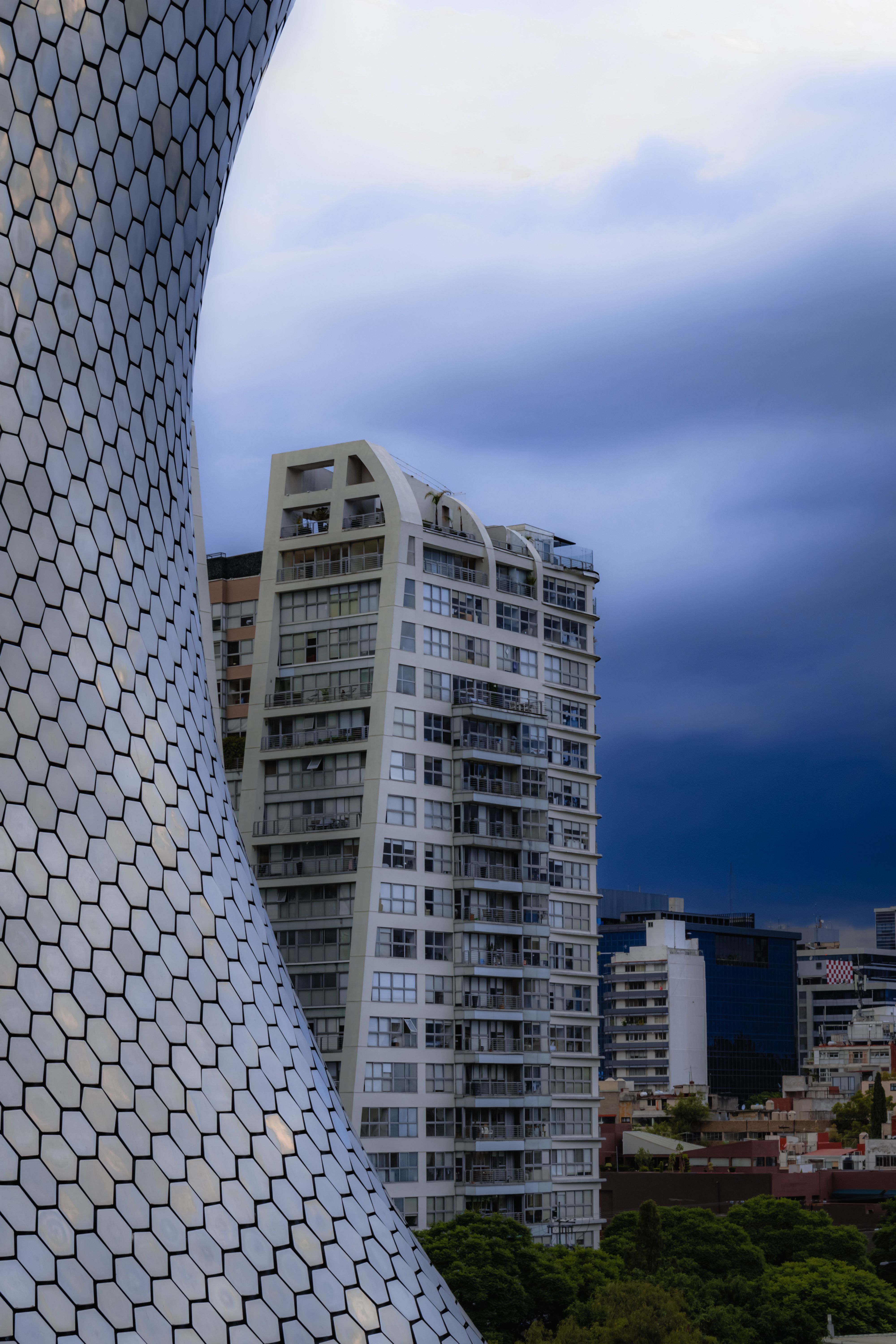 A striking view of a modern skyscraper alongside a uniquely curved architectural structure under a dark sky.