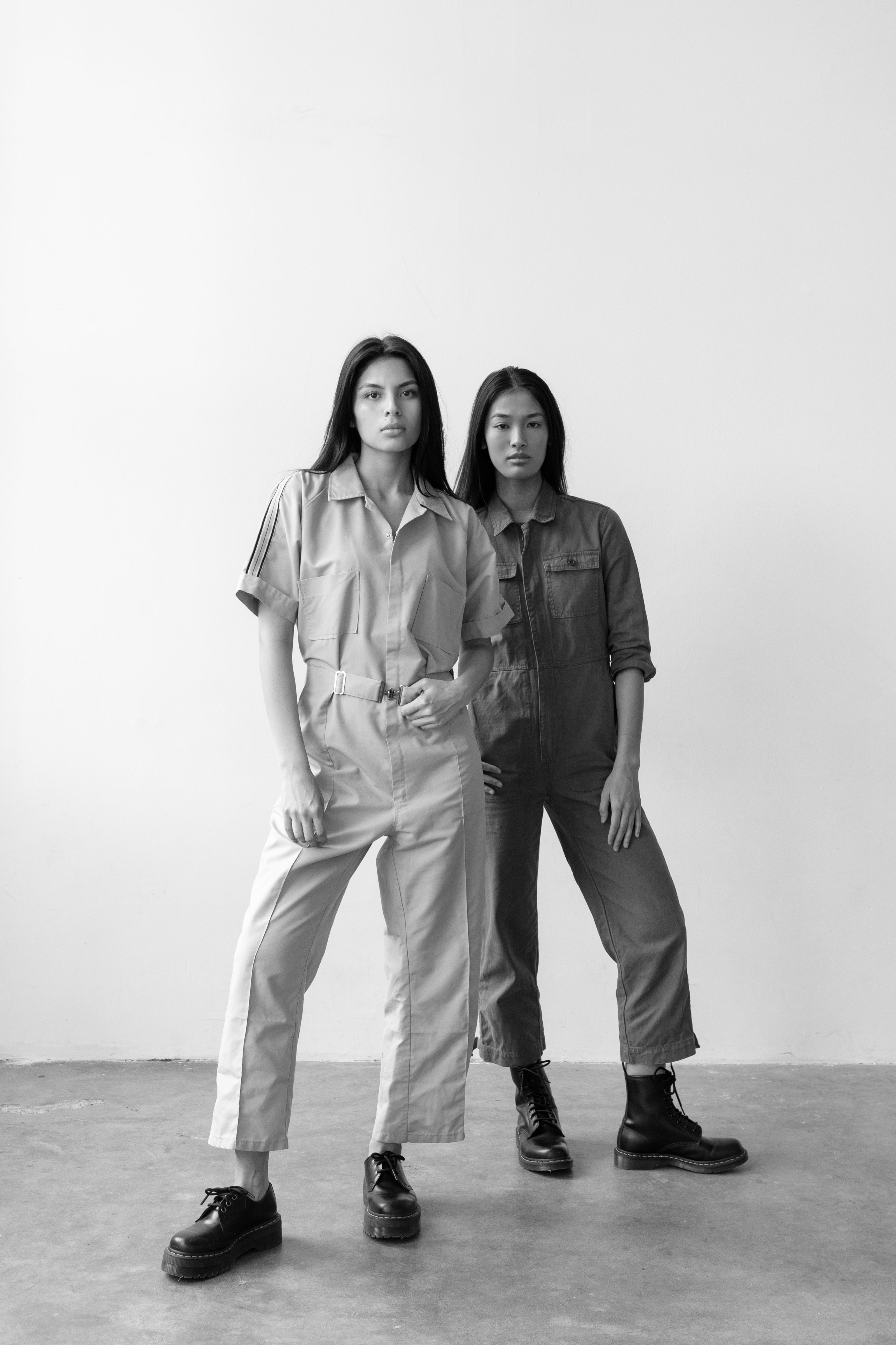 Retrato estiloso em preto e branco de duas mulheres em macacões posando em um estúdio.