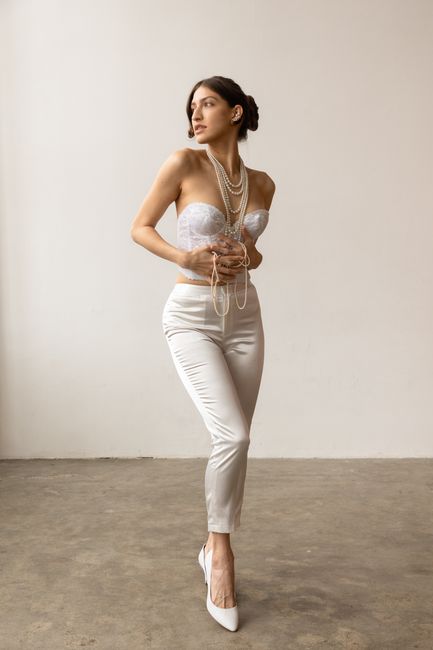 A fashionable woman posing in a white outfit adorned with pearls, standing in a studio setting.
