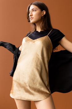 Studio portrait of a woman posing confidently in a stylish dress over a brown background.