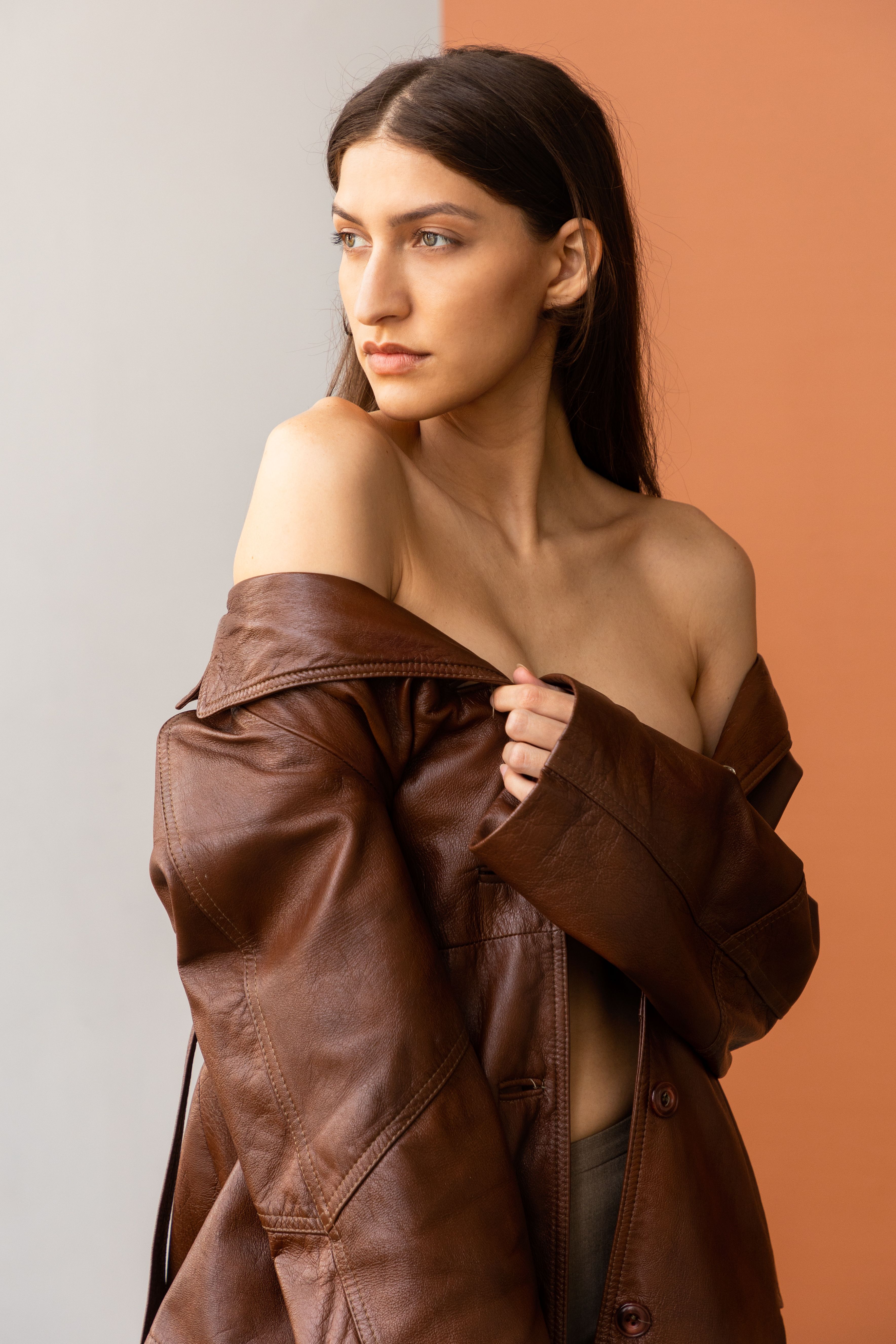 A sophisticated fashion portrait of a woman wearing a leather coat, posed against a warm backdrop in a studio setting.