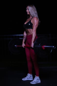 Athletic woman lifting a barbell during a nighttime workout session, showcasing fitness and strength.