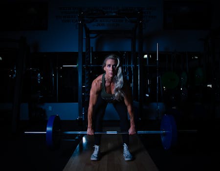 A fit woman lifting a barbell in a dimly lit gym, showcasing strength and determination.