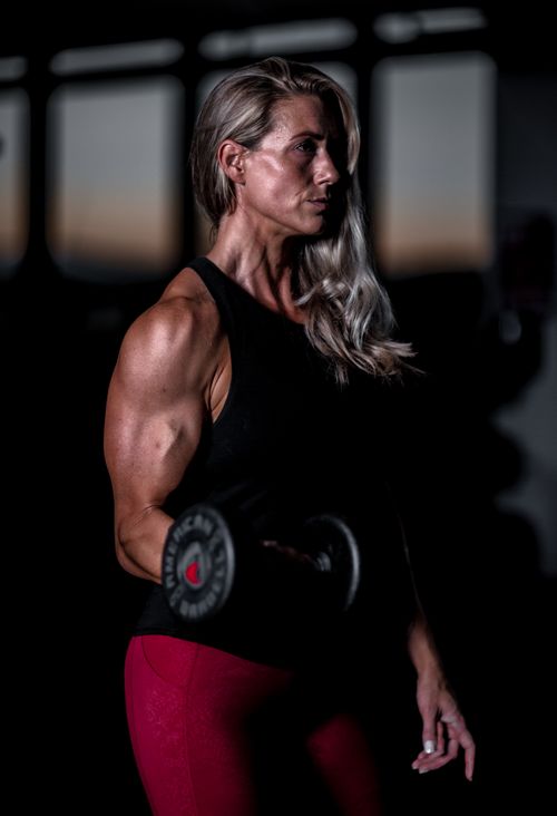 Free A fit woman lifts a dumbbell in a dimly lit gym, showcasing strength and dedication. Stock Photo