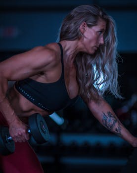Strong athletic woman lifting dumbbells in a dimly lit gym, showcasing strength and fitness.