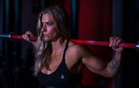 Muscular woman in a gym lifting a barbell, showcasing strength and focus in fitness.