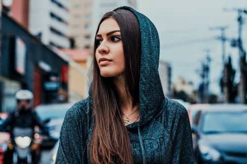 Free Stylish young woman in a hoodie on a bustling city street, showcasing urban fashion. Stock Photo