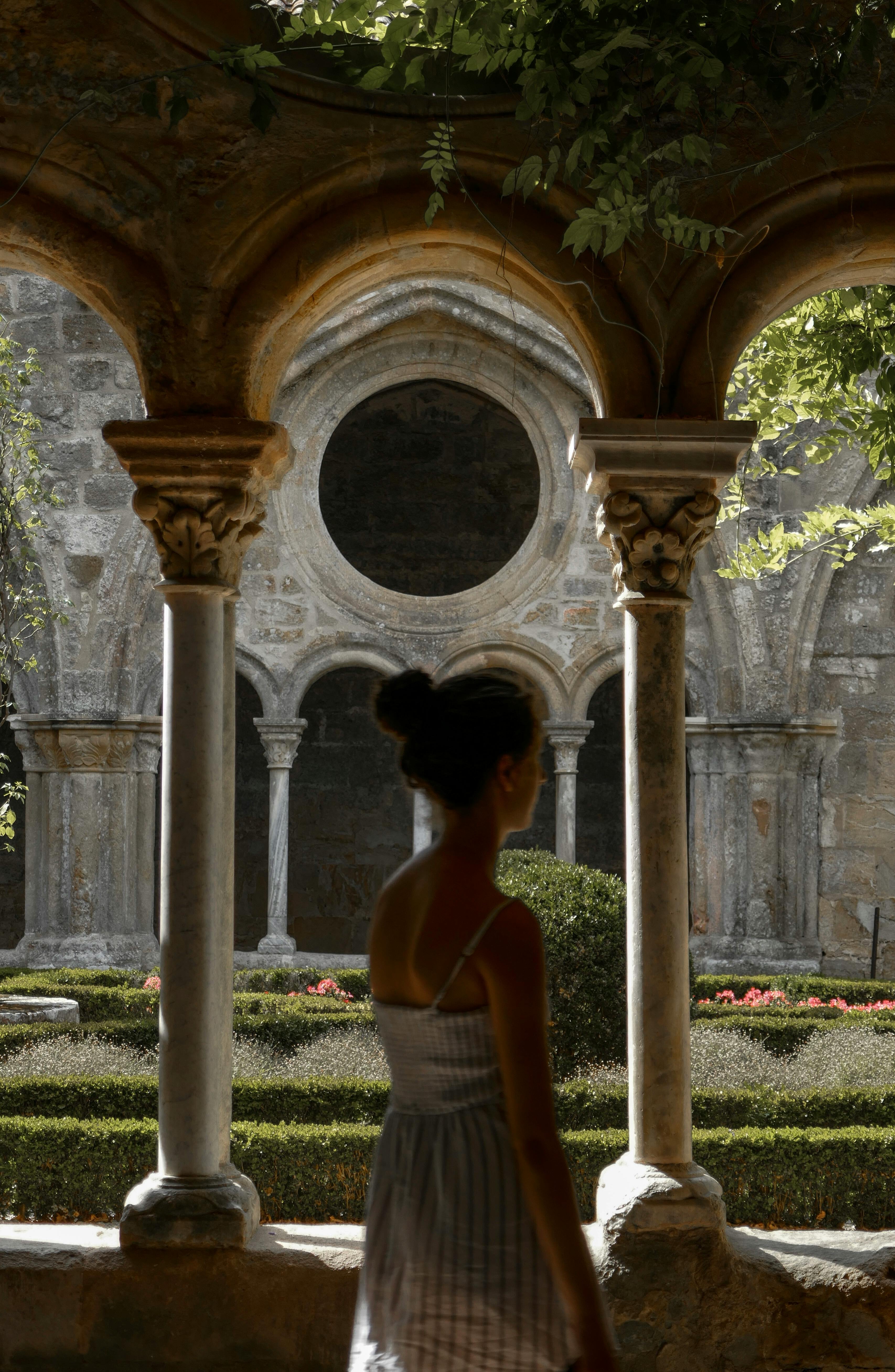 Woman walking through a historic monastery cloister garden under ancient arches.