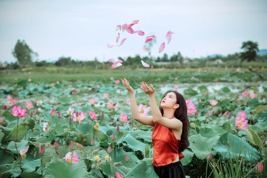 一个成年女子在阳光明媚的日子里，于充满活力的莲花花园中享受着飘落的花瓣