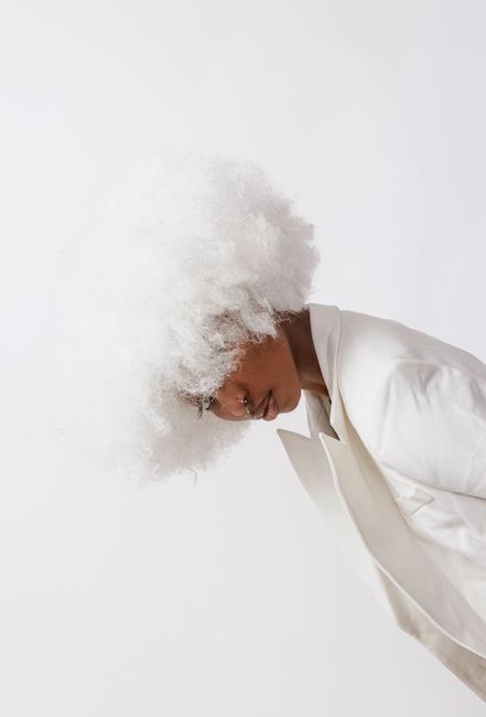 Stylish African American woman in white outfit with curly wig against white background in studio.