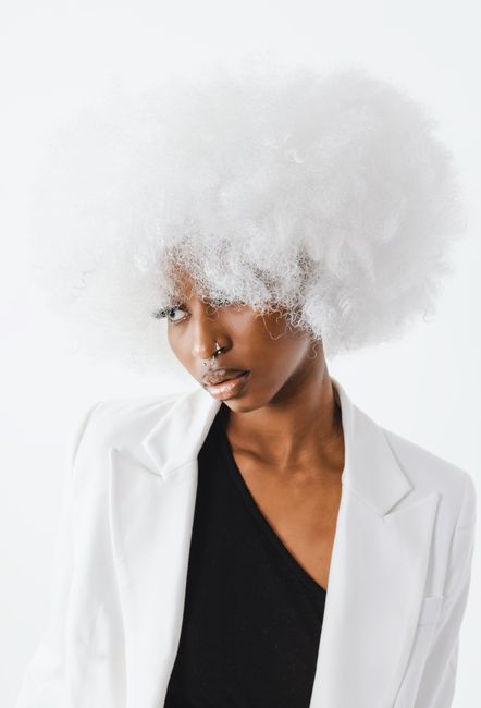 Elegant studio portrait of a fashionable woman with a fluffy white afro wig and chic attire.