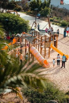 Children and adults enjoy a sunny day at a vibrant playground with slides and climbing structures.