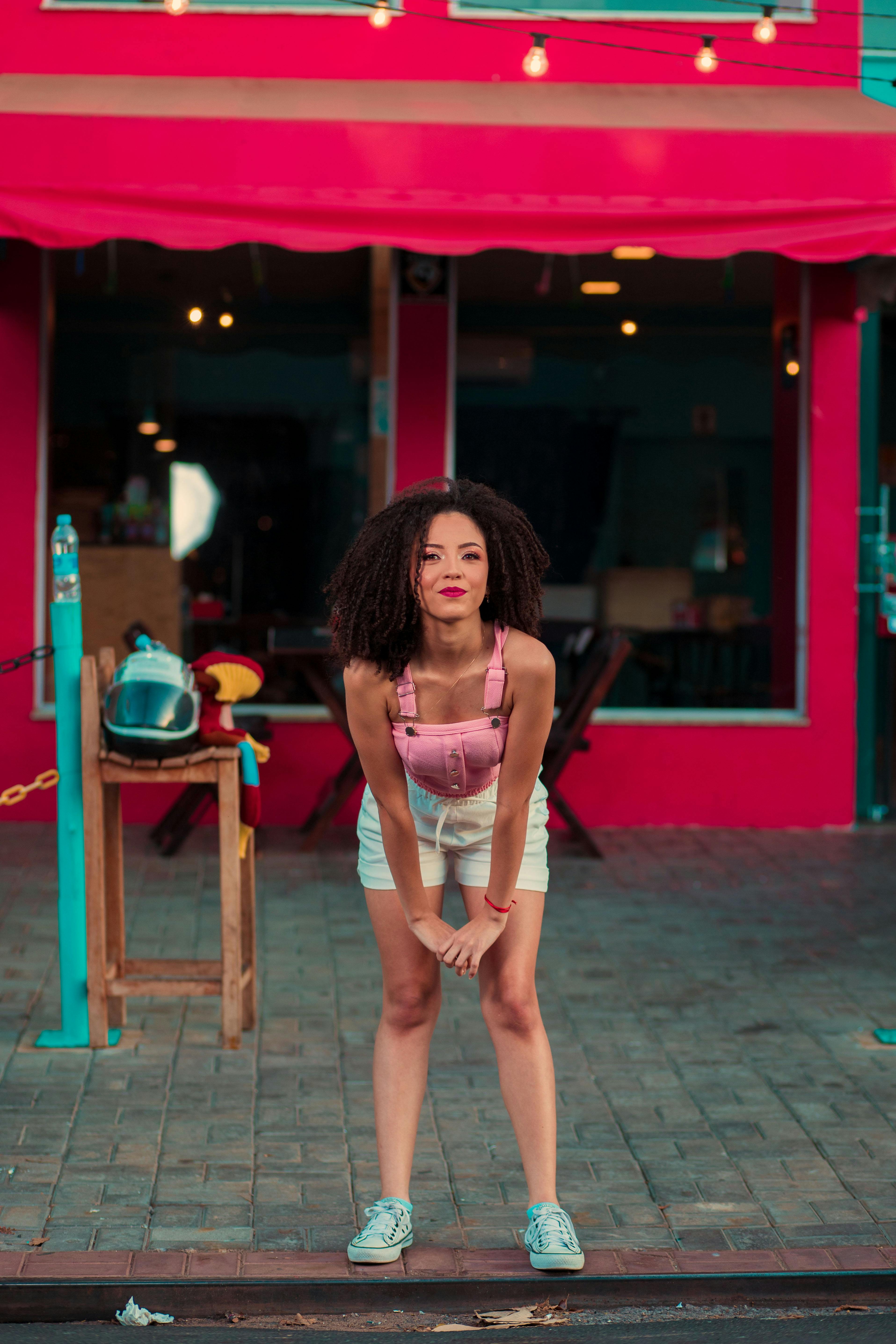 Free Photo  Pensive woman in pink shorts looking down. outdoor shot of  tanned female model sitting on bricked wall.