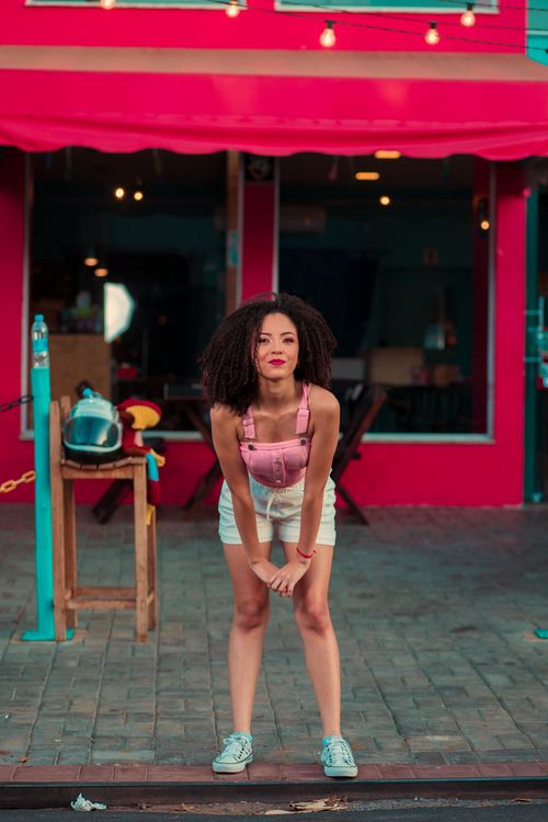 Free Smiling woman in pink top with afro hair posing playfully on a sidewalk. Stock Photo
