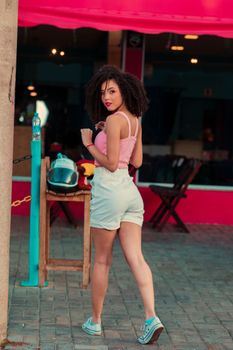 Fashionable woman in a pink tank top and white shorts posing stylishly on a city sidewalk.