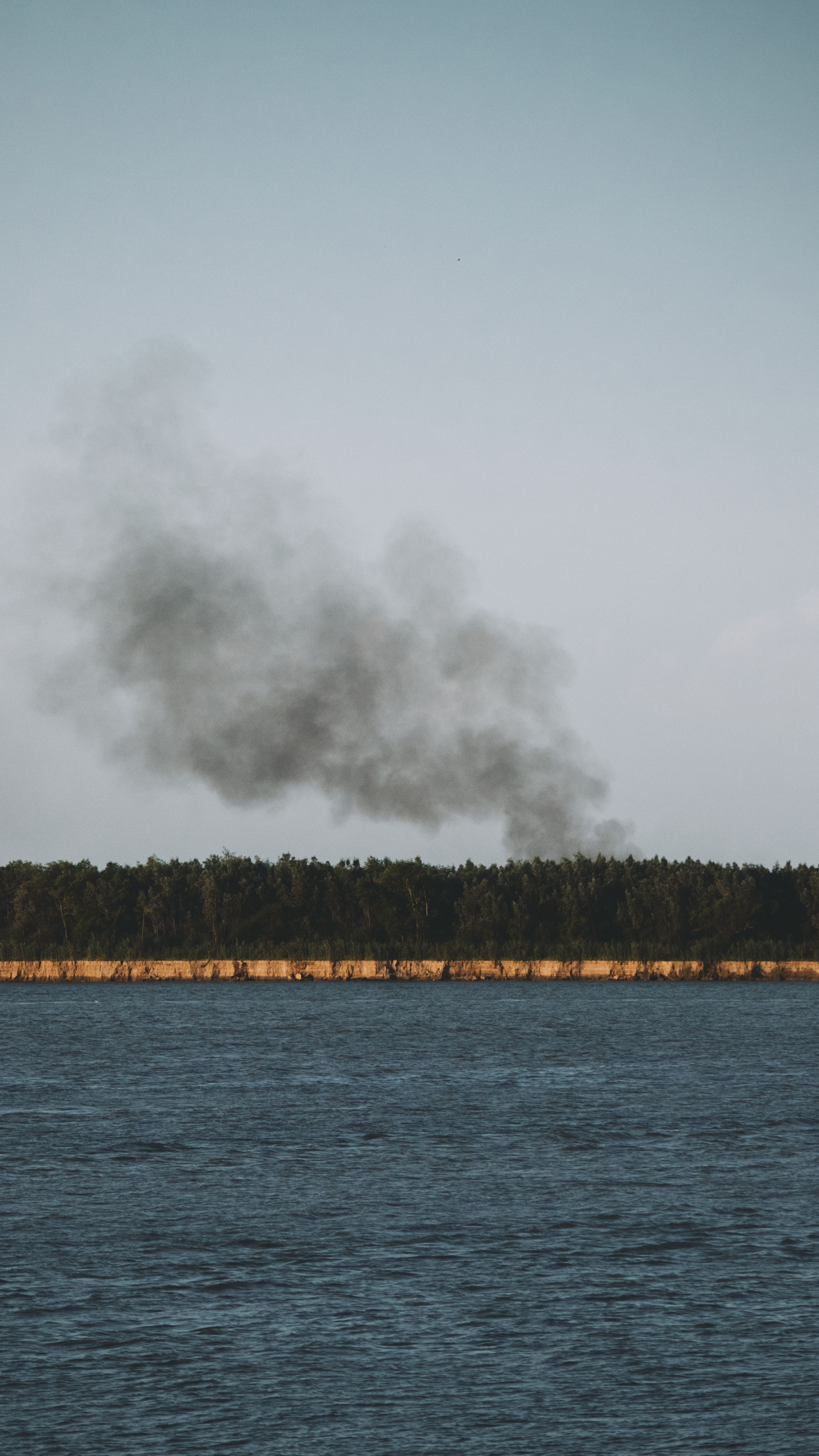 A Black Smoke Rising in the Air Near Body of Water · Free Stock Photo