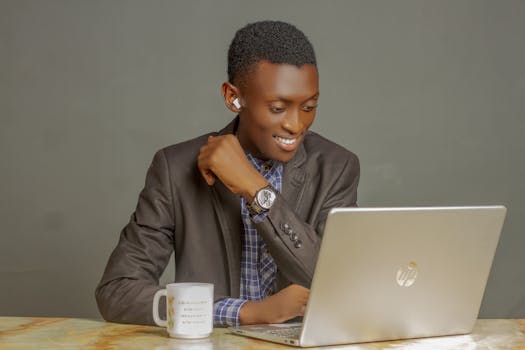 Young man in a suit smiling while video calling on a laptop indoors.