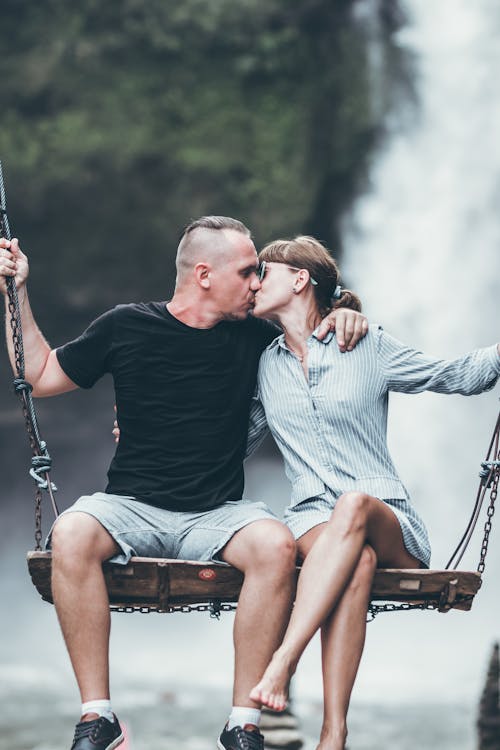 Man And Woman Sitting On Wooden Swing While Kissing