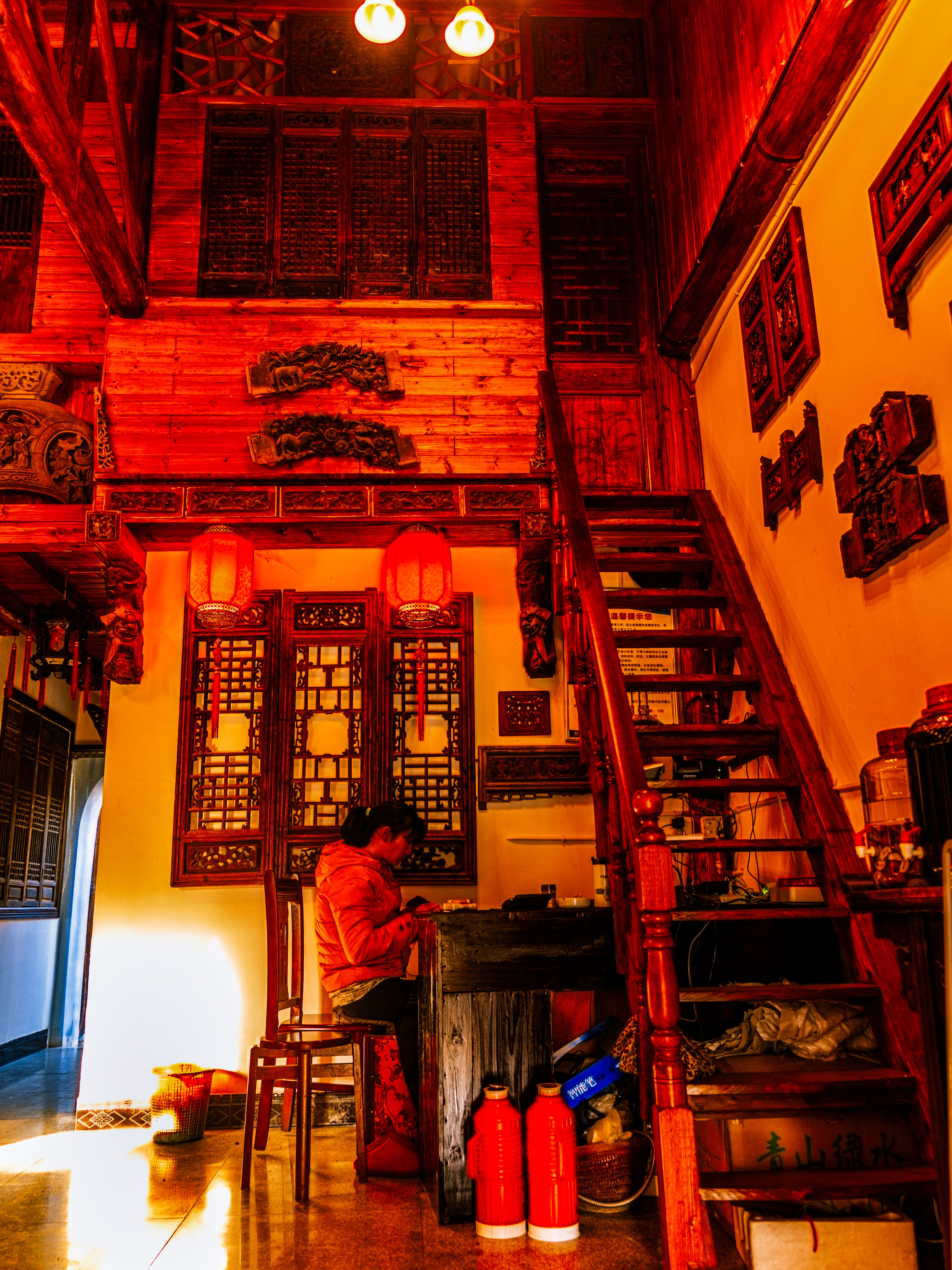 A cozy room with Chinese lanterns and wooden stairs, featuring a person seated at a table.