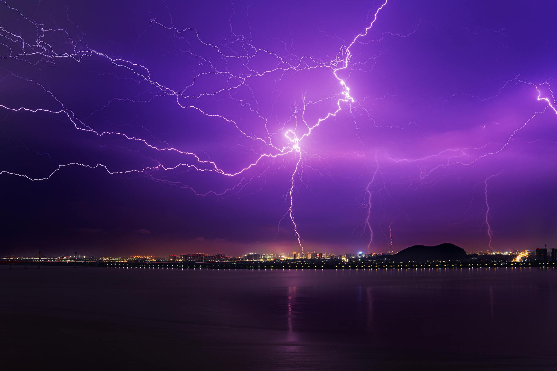 Vibrant lightning strikes over a city skyline with a purple sky, capturing the intensity of a thunderstorm.