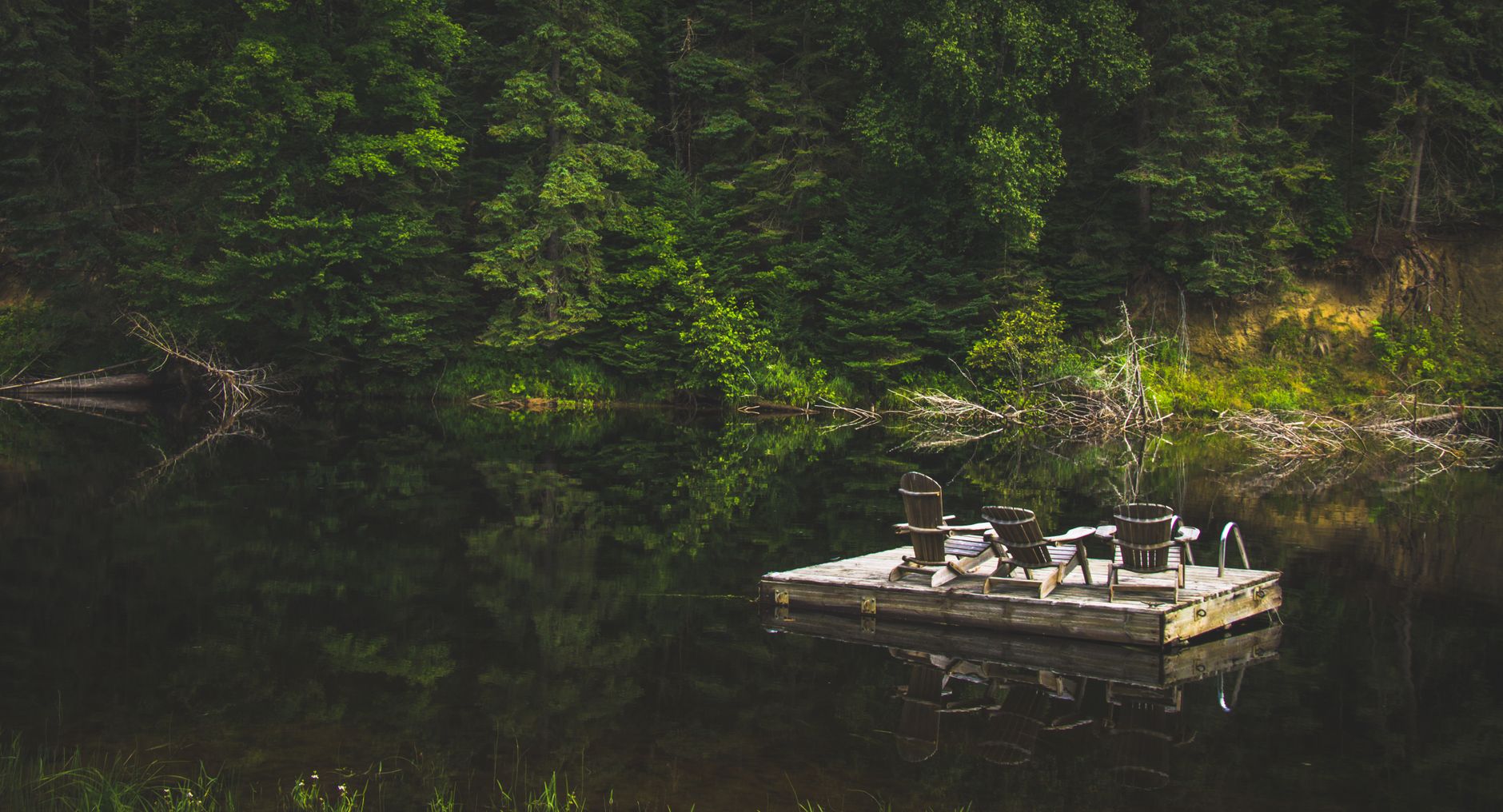 Tranquil summer scene of a wooden dock with chairs on a reflective lake in Bracebridge, Canada.