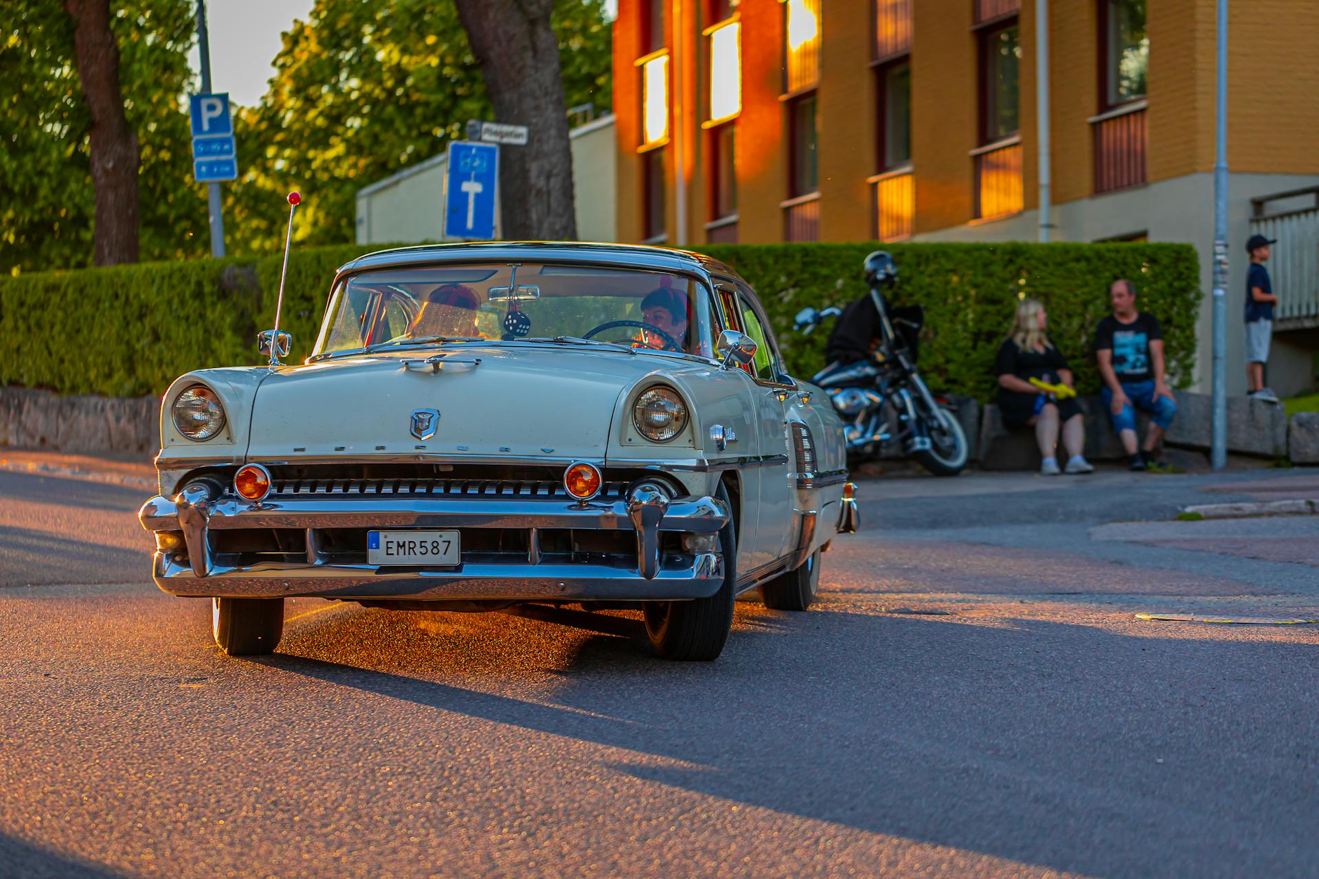 A classic beige Mercury Montclair drives on a sunny urban street, capturing vintage automotive charm.