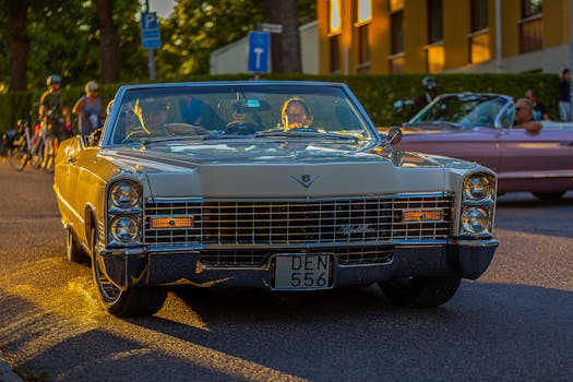 A vintage Cadillac convertible cruising down a sunlit street with people enjoying the ride.