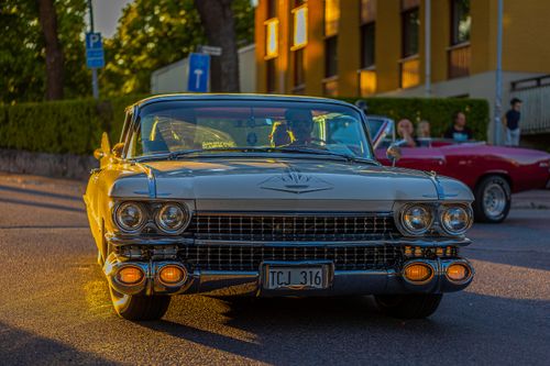 Free A vintage beige Cadillac driving on a city street at sunset, capturing nostalgic charm. Stock Photo