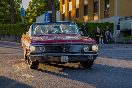 A classic red Buick LeSabre drives through city streets at sunset, capturing the retro charm of vintage cars.