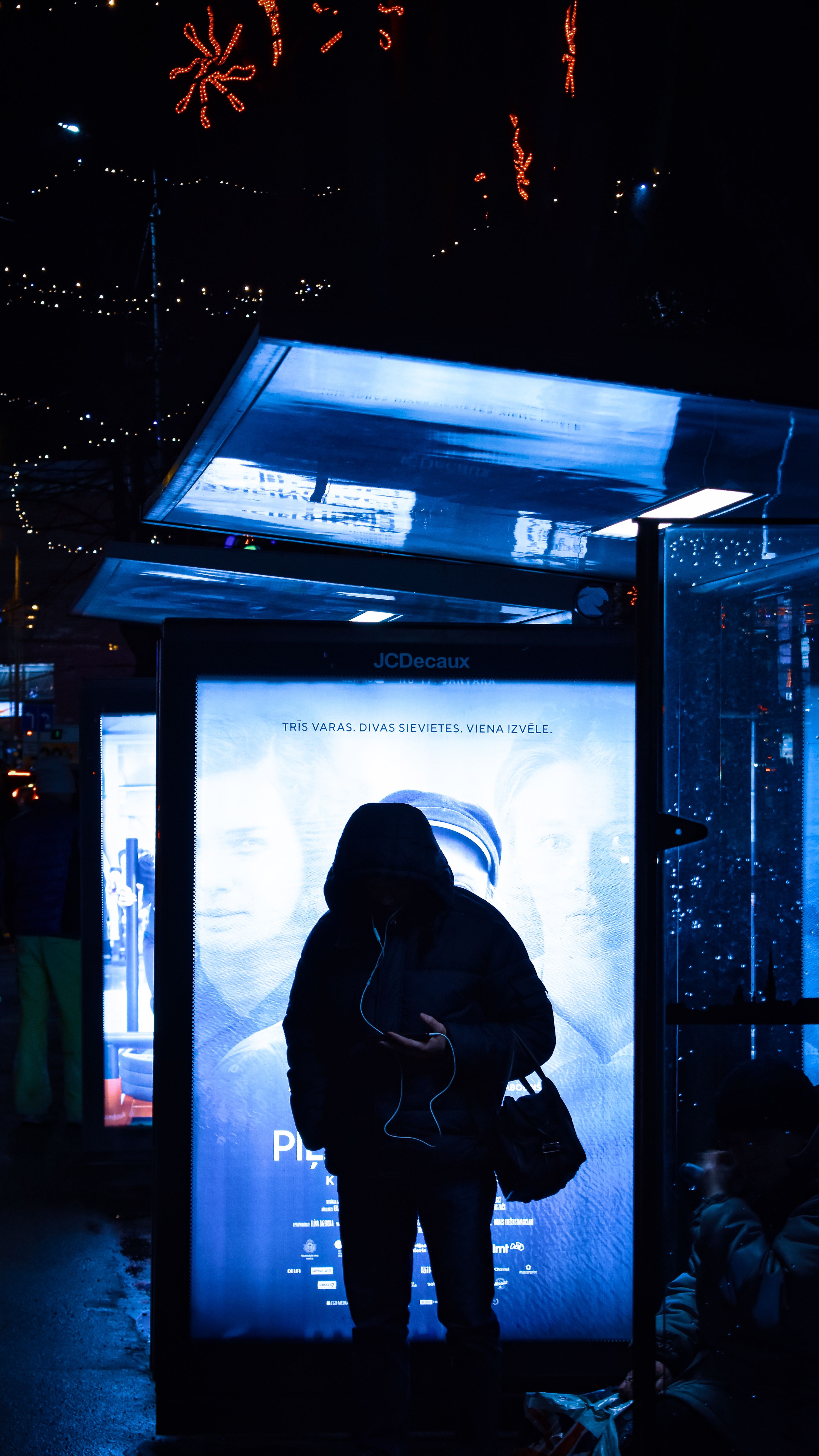 A silhouetted person in front of illuminated signage at a nighttime bus stop.