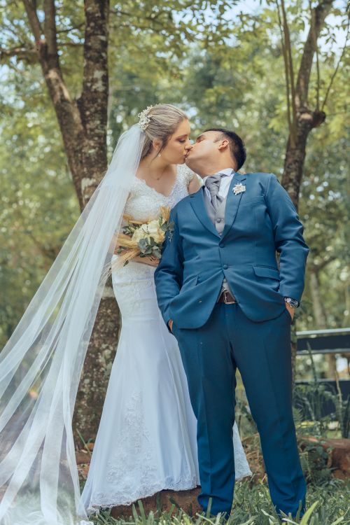Free A bride and groom share a tender kiss amidst a serene, green outdoor setting. Stock Photo