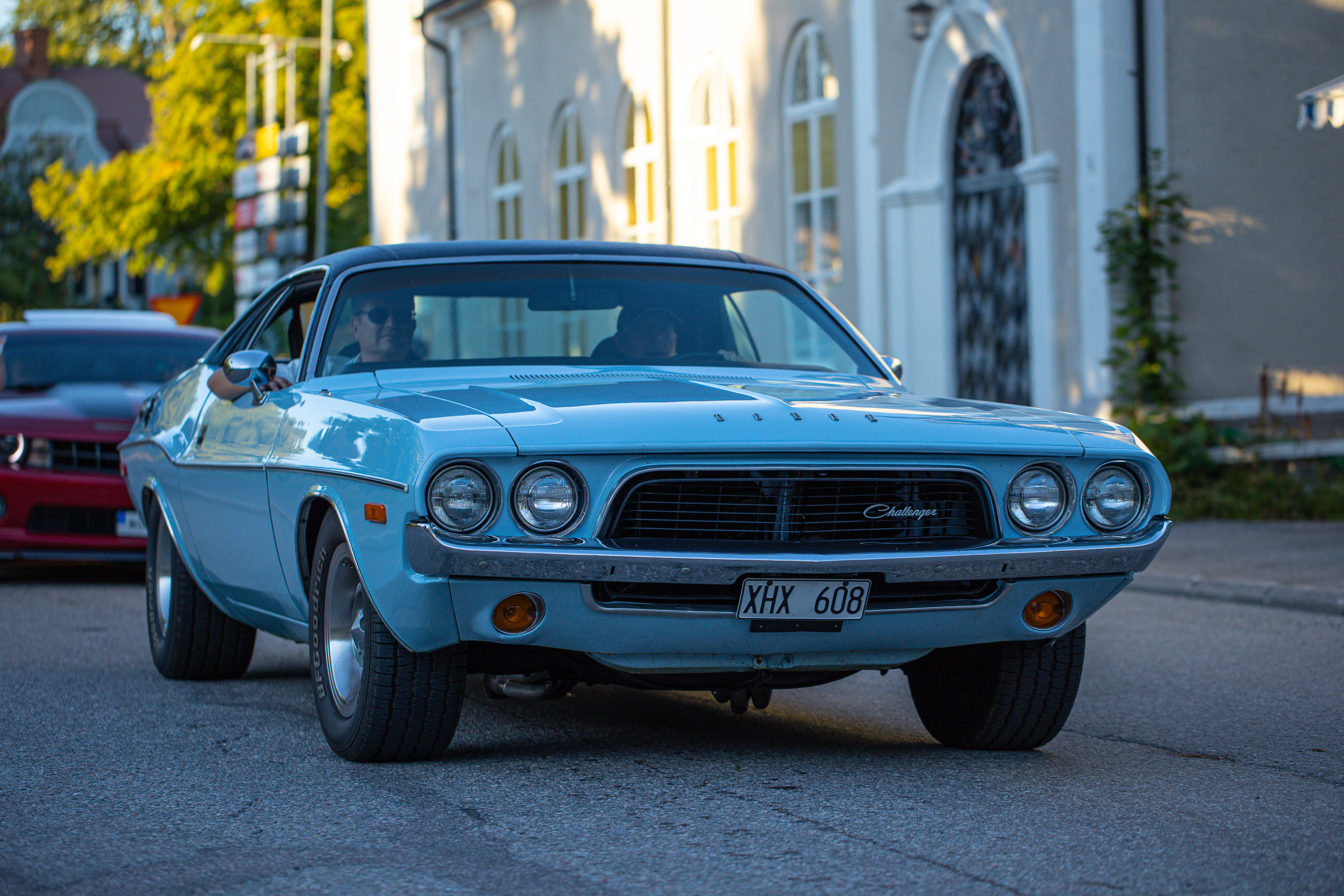 Vintage blue Dodge Challenger driving on a sunlit urban street, showcasing classic car beauty.