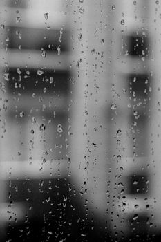 Raindrops trickling down a window with an Istanbul cityscape in grayscale.
