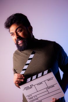 Bearded man showing intense emotion with a clapperboard in a studio setting.