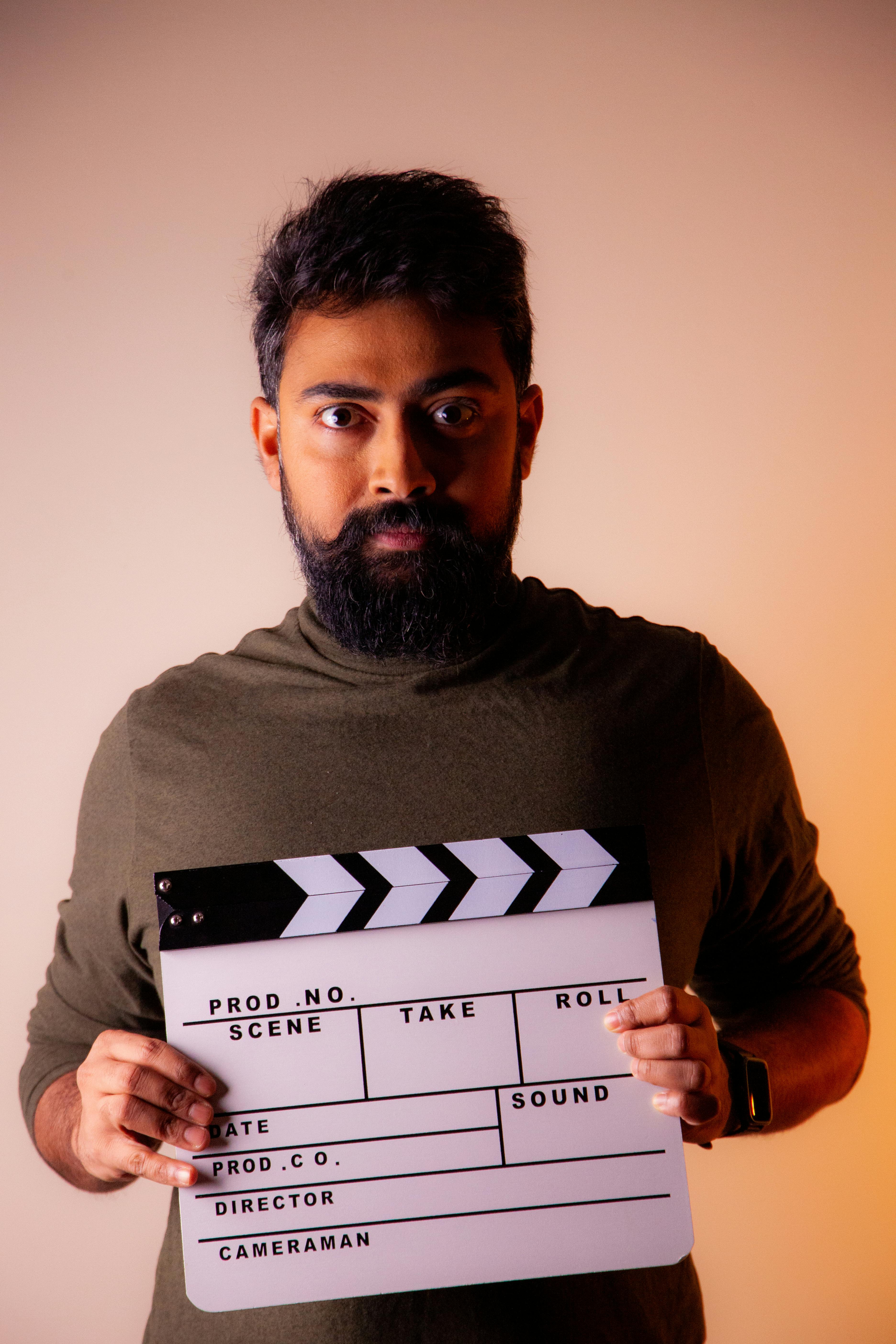 Studio portrait of a man with beard holding a clapperboard, highlighting filmmaking theme.