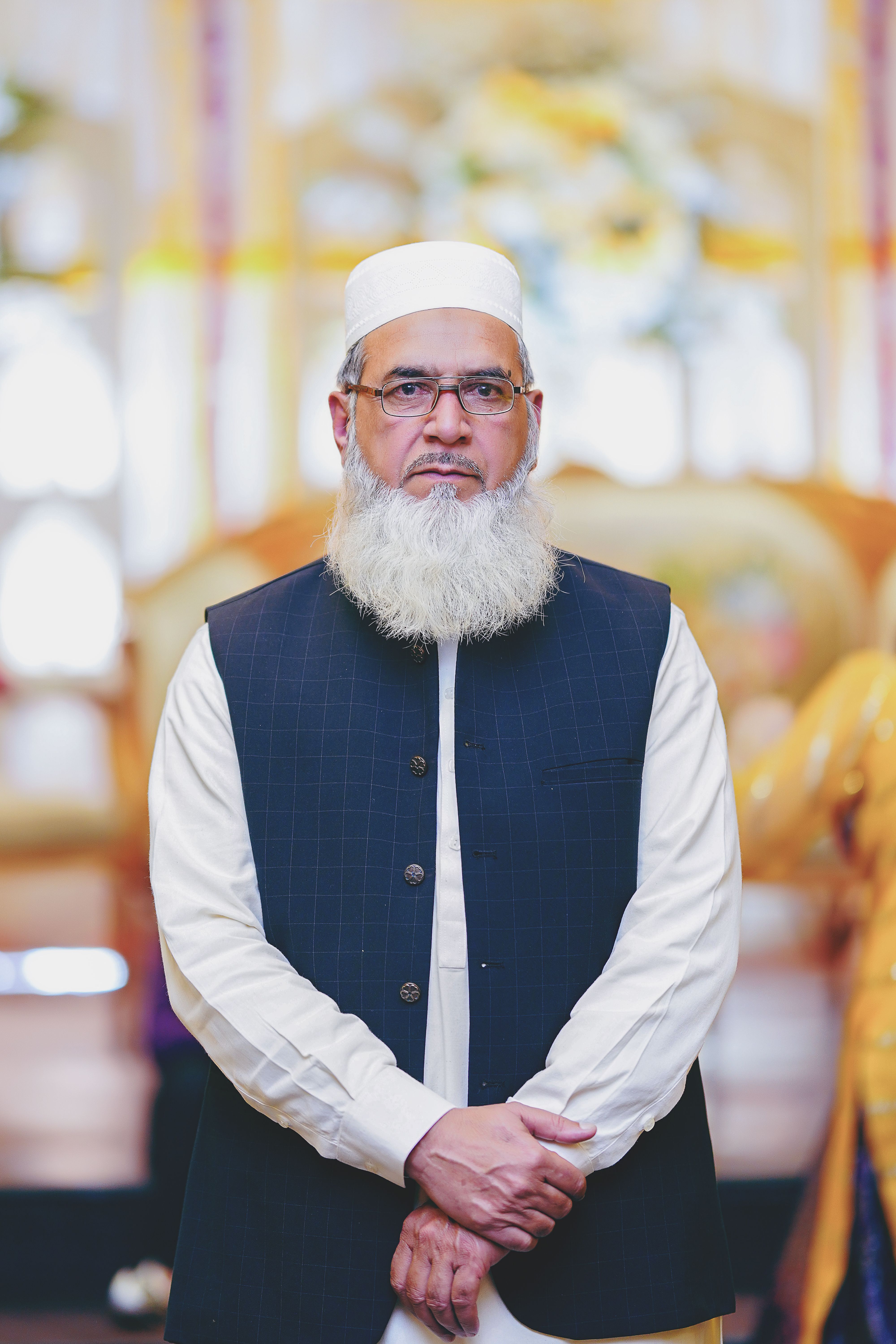 Portrait of an elderly man with a beard wearing traditional clothing and kufi indoors.
