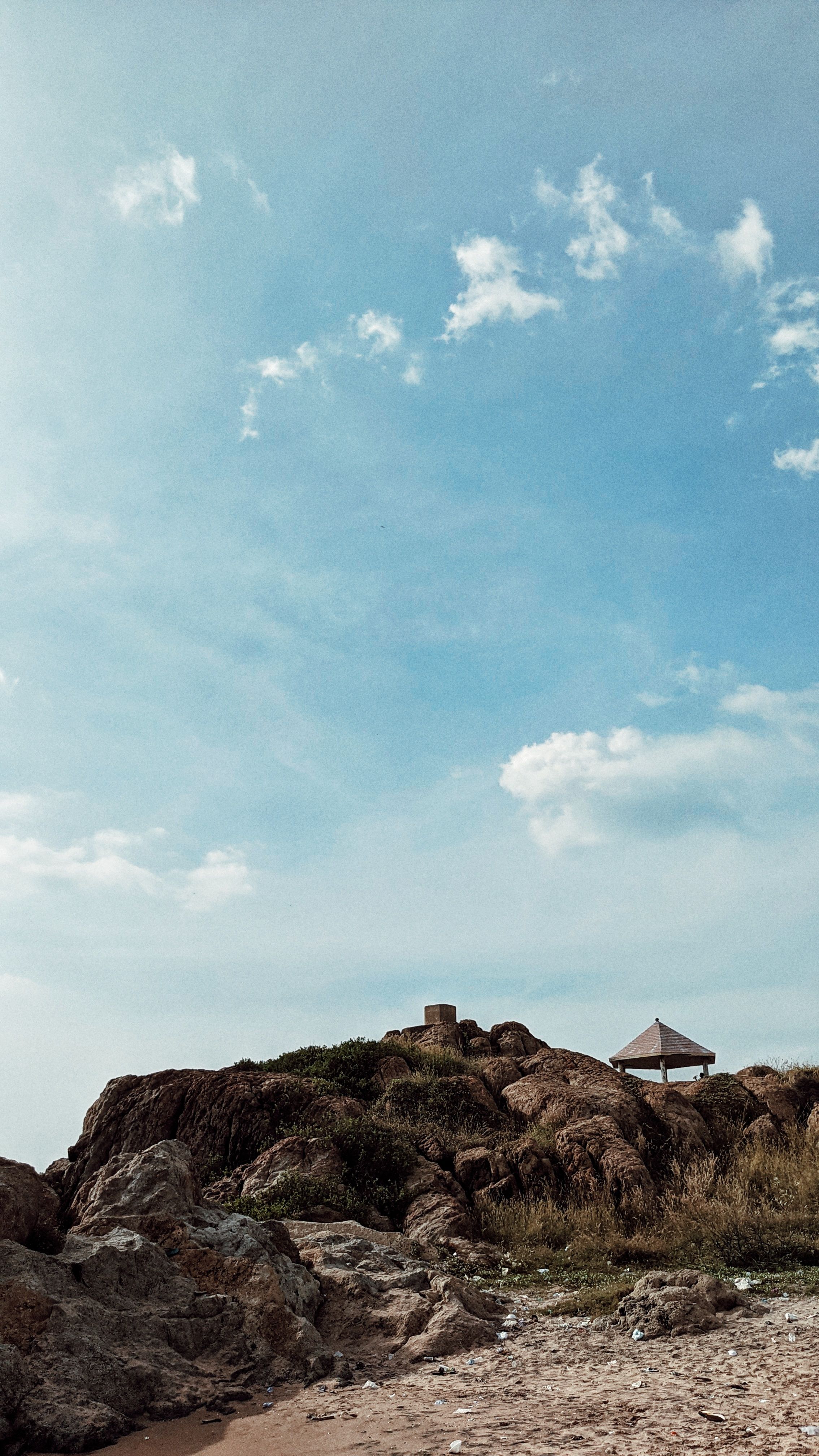 A tranquil summer landscape of a rocky hill with a distant gazebo under a clear blue sky.