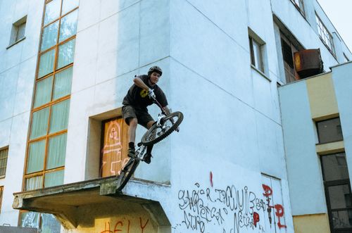 Free A man performing a bicycle trick on an urban ledge with graffiti in a city environment. Stock Photo