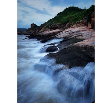 A mesmerizing long exposure capture of ocean waves crashing onto a rocky coastline under a cloudy sky.