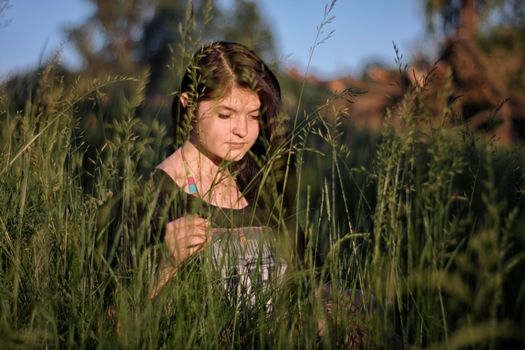 A young woman in a field of tall grass, enjoying the warm sunlight during summer in Kharkiv, Ukraine.