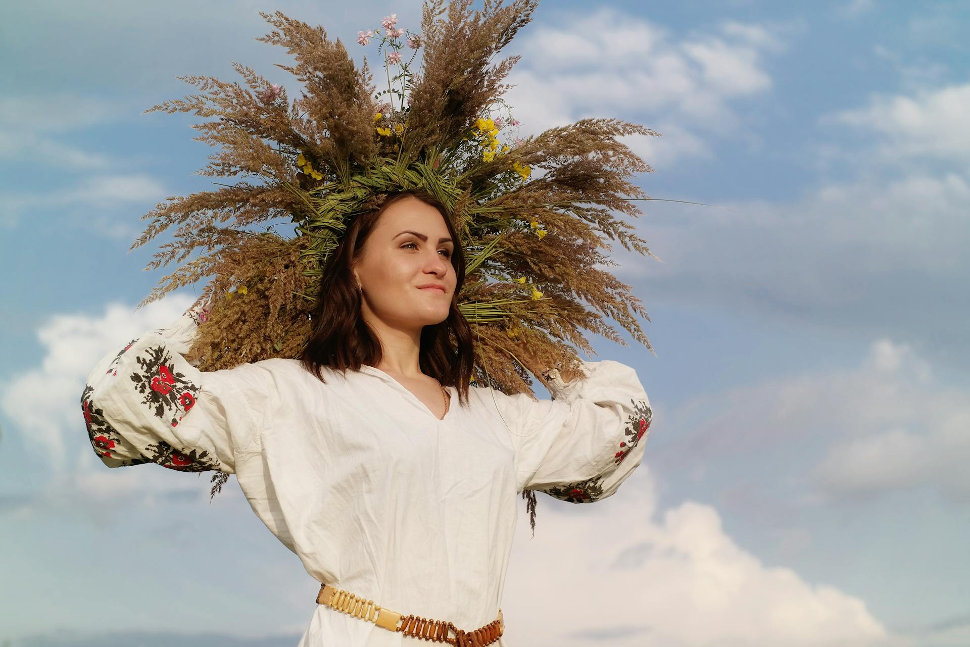 A Ukrainian woman in traditional dress with a floral crown poses confidently against a bright blue sky.