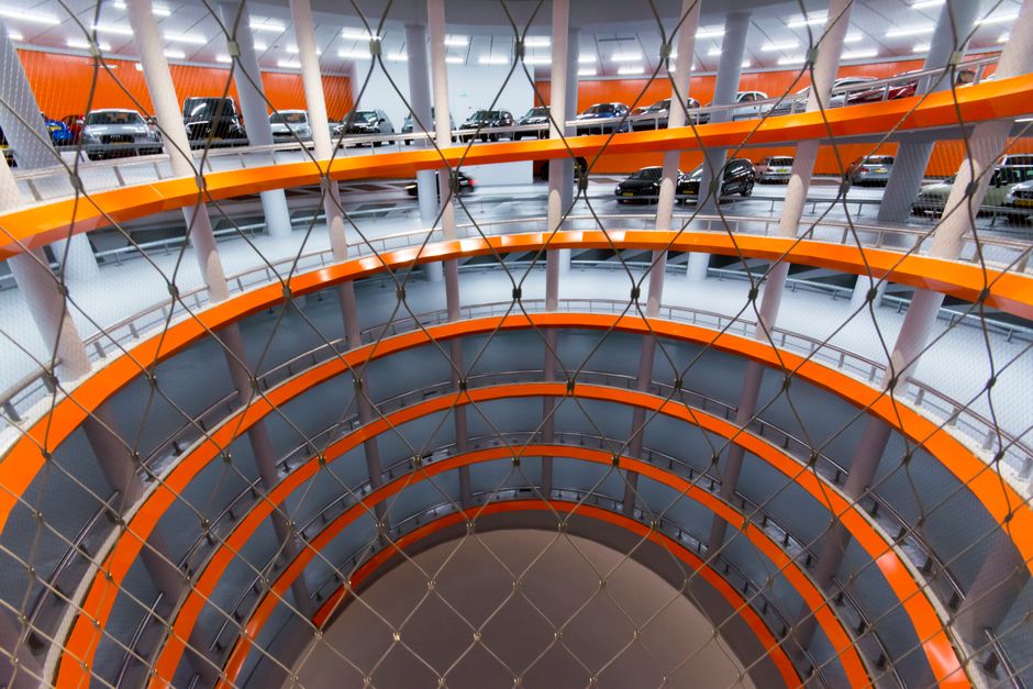 Dramatic spiral view of a modern multi-level indoor car parking garage with vibrant orange accents.